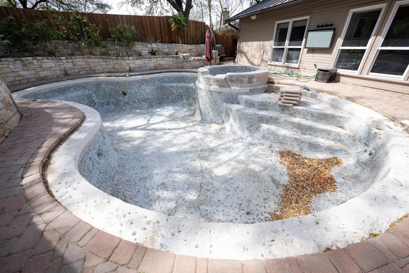 Wide view of a drained pool and spa with old plaster and brick coping