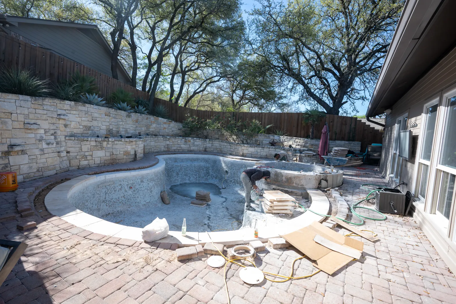 Drained freeform pool and spa with new travertine coping set around the edge and a paver deck beyond it