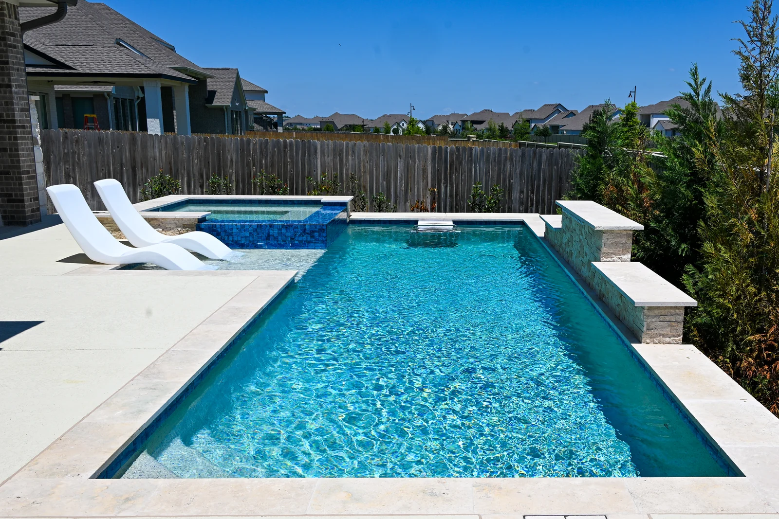 Modern rectangular gunite pool with a raised spa and white loungers on the tanning ledge