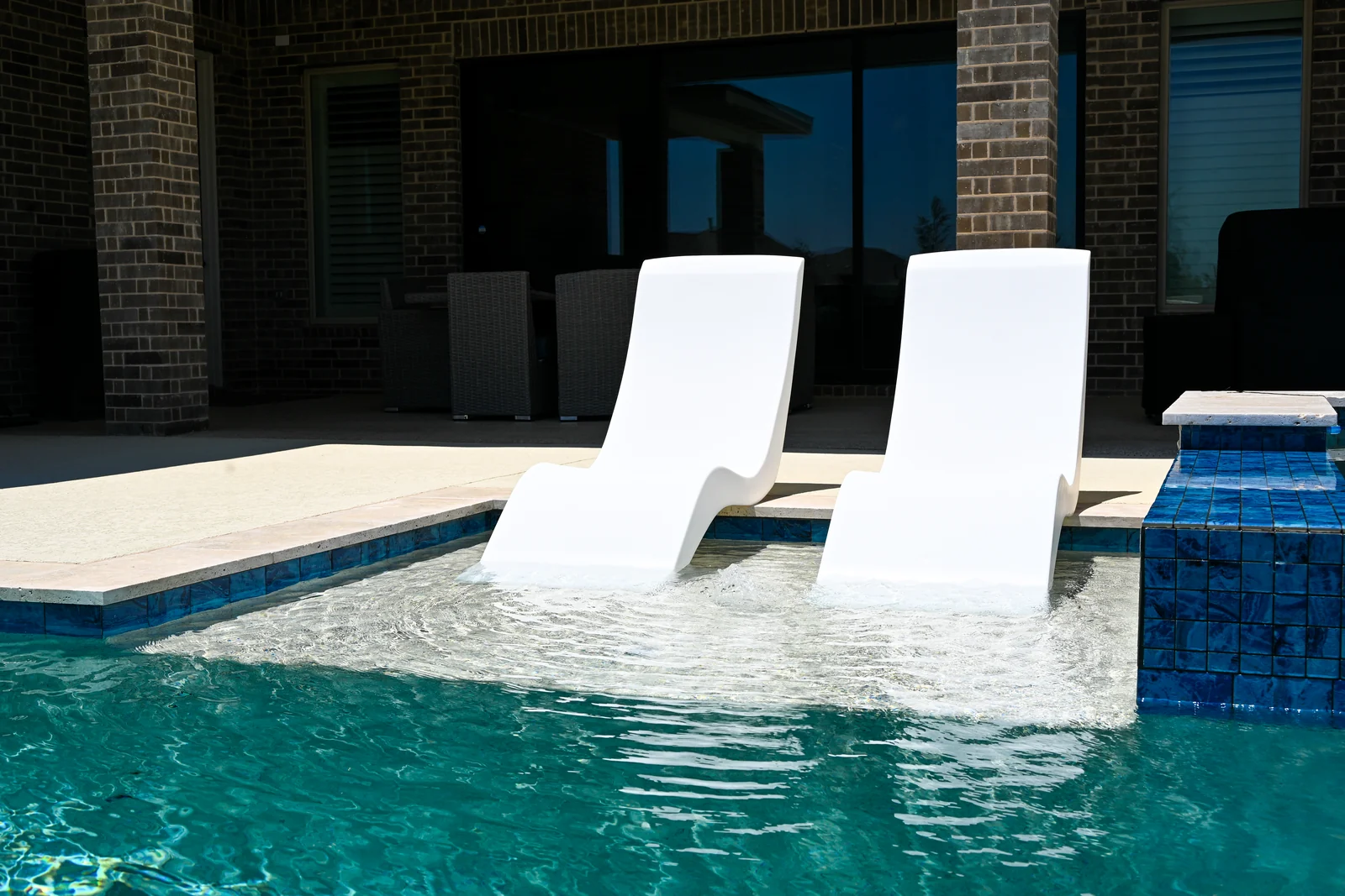 White in-water loungers on a tanning ledge with the house behind