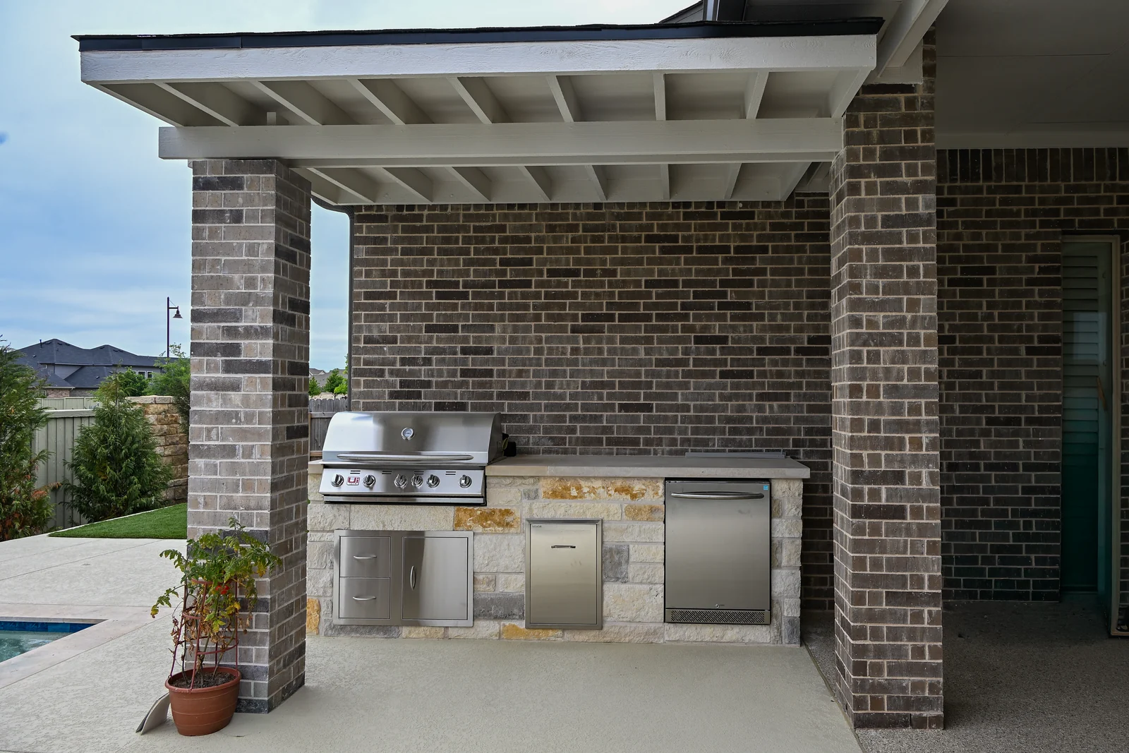 Covered outdoor kitchen with built-in grill under a brick pergola