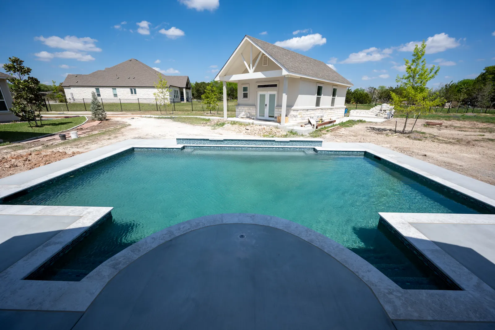 Rectangular pool with light stone coping and a new pool house behind it