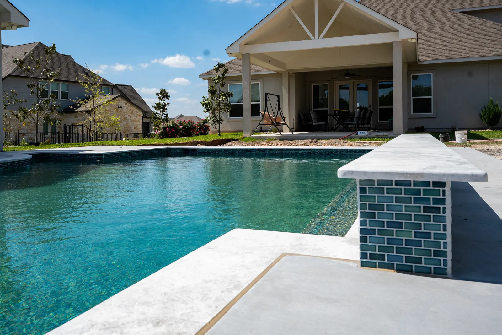 Raised wall faced in teal glass tile beside a pool