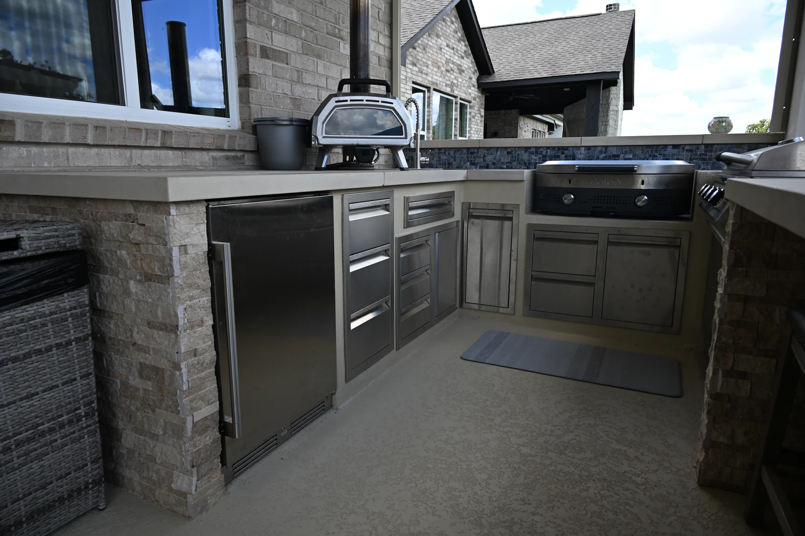 Covered outdoor kitchen with a built-in grill and stone counter beside a pool