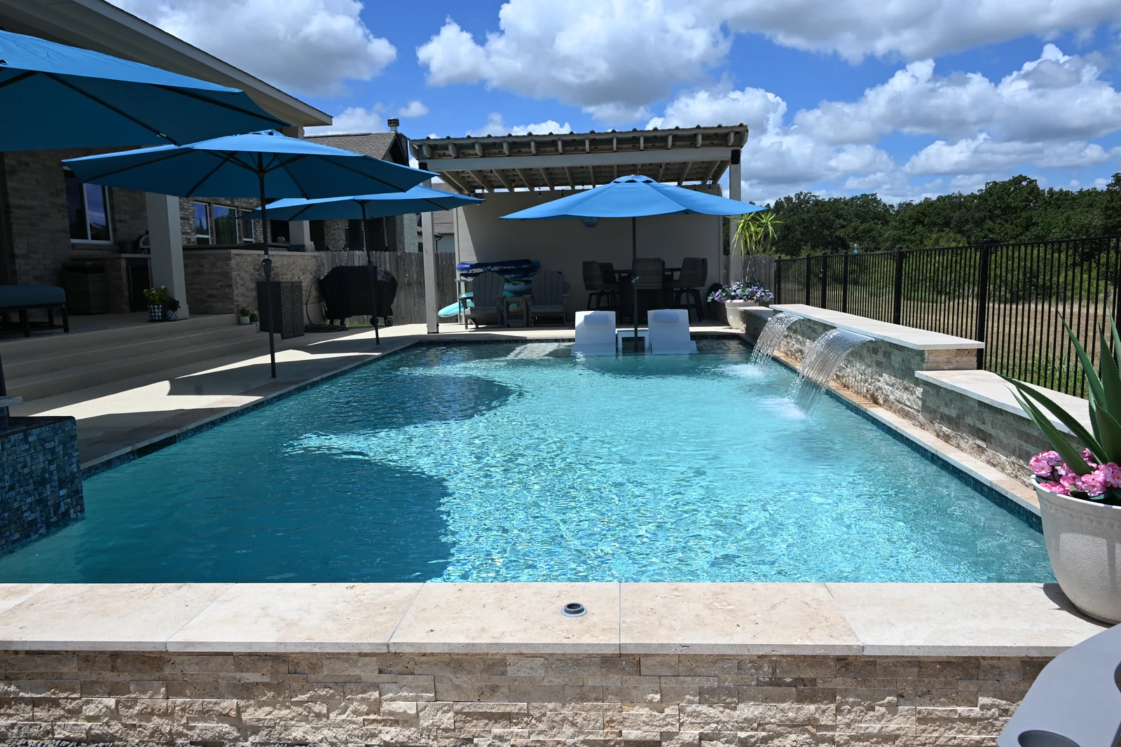 Rectangular pool with a raised spa, pergola and outdoor kitchen behind it