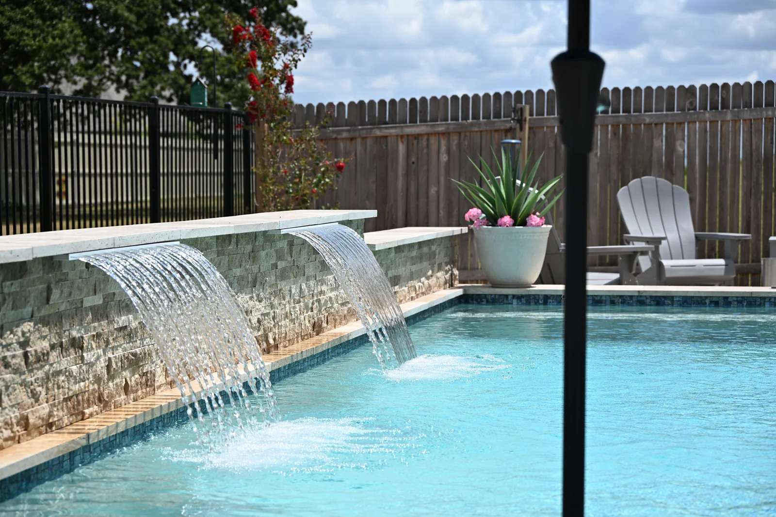 Stacked-stone spillway wall running the length of a pool, planter and fence beyond